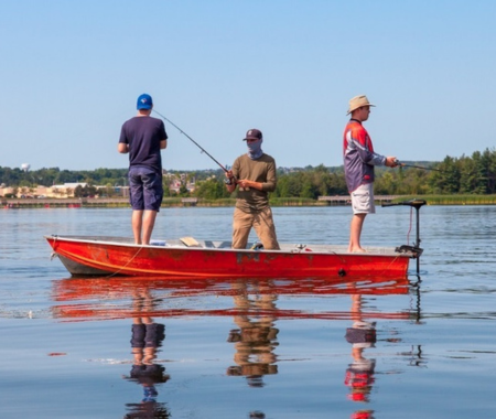 Three people holding fishing rods are standing in a boat on water.